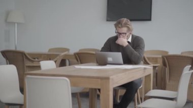 Netbook önünde hafif rahat bir ofiste masada oturan gözlük portre başarılı sarışın düşünceli adam. Yakışıklı işadamı çalışma sürecinde yer alıyor. Kamera sağa doğru hareket eder