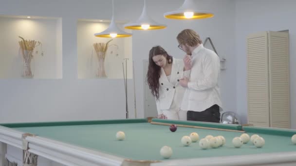 Blonde bebaarde man leert zijn vriendin om biljart te spelen. Zelfverzekerde man in wit shirt legt de vrouw in elegant pak uit hoe pool te spelen. Biljart sport concept — Stockvideo