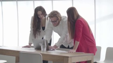 Gözlükyakışıklı sarışın adam kadın meslektaşlarına bilgi gösteren hafif rahat bir ofiste netbook üzerinde eğildi. Patronun her iki tarafında duran resmi giyim iki kadın