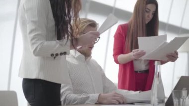 Portre sinir adam masada netbook ile modern ofiste oturan iki kadın meslektaşları ona birer birer verir belgeleri toplama, sonra kağıt yığını atmak.