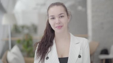 Portre sevimli iş kadını kameraya bakarak hafif rahat bir ofiste ayakta. Ofis alanında işyerinde başarılı kendine güvenen kız.