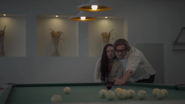 Successful blond bearded man teaches his girlfriend to play billiard. Confident man in white shirt explains to the woman in elegant suit how to play pool. Billiard sport concept — Αρχείο Βίντεο