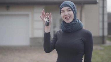 Geleneksel başörtüsü takan araba anahtarlarını tutan ve sallayan bağımsız gülümseyen genç Müslüman kadın portresi