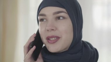 Siyah başlık genç bir güzel Müslüman kadının portresi cep telefonu ile yakından konuşurken. Başörtülü sevimli asyalı kız kameraya bakıyor.