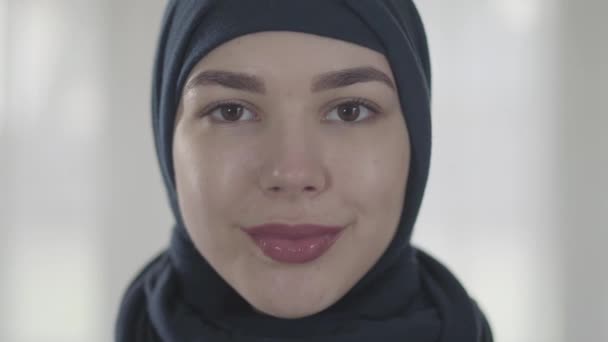 Retrato de uma jovem mulher oriental sorridente na roupa muçulmana moderna e bela cobertura para a cabeça preta de perto. Jovem asiático muçulmano mulher na cabeça cachecol olhando na câmera — Vídeo de Stock