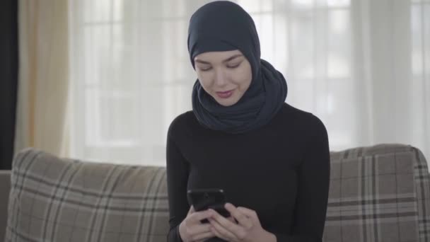 Retrato de una joven musulmana independiente escribiendo un mensaje usando un teléfono inteligente con un pañuelo tradicional — Vídeo de stock