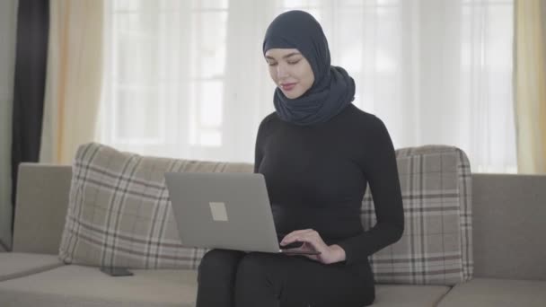 Wanita muslim muda bekerja atau mengobrol dengan laptop dan setelah seseorang memanggilnya dengan smartphone — Stok Video