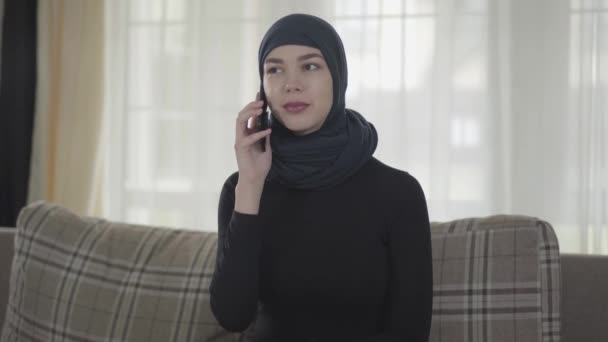 Retrato de una joven musulmana seria e independiente que habla con un teléfono inteligente con un pañuelo tradicional — Vídeos de Stock