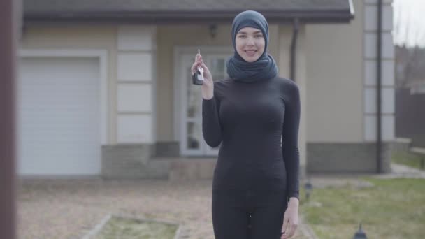 Retrato de una joven musulmana sonriente e independiente sosteniendo y agitando las llaves del coche con un pañuelo tradicional — Vídeos de Stock