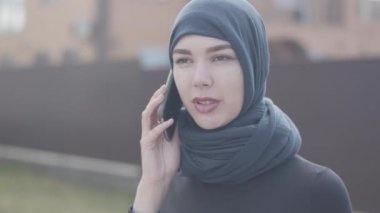 Siyah giysiler ve güzel başlık cep telefonu yakından konuşan genç bir doğu kadının Portresi. Türbanlı Asyalı kadın yeni bir ev satın aldı.