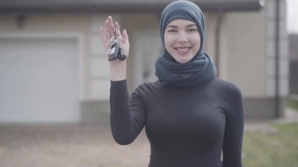 Porträtt av oberoende framgångsrika trygg leende ung muslimsk kvinna Holding och vinka bilnycklar bär traditionella huvudduk utomhus. — Stockvideo