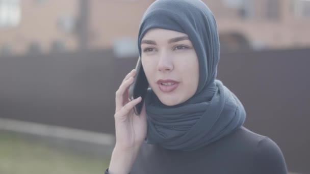 Porträt einer jungen Ostfrau in schwarzer Kleidung und schönem Kopfschmuck, die per Handy aus nächster Nähe spricht. Asiatin mit Kopftuch kaufte sich ein neues Zuhause. — Stockvideo