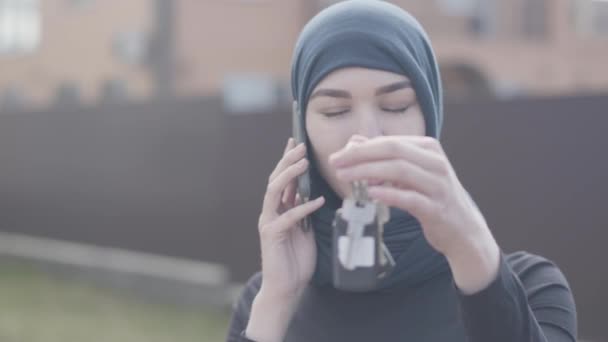 Portrait de jeune femme musulmane souriante indépendante parlant bey téléphone et tenant des clés de voiture portant le foulard traditionnel — Video