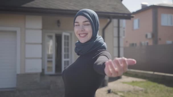 Porträt einer unabhängigen jungen muslimischen Frau, die lächelt und flirtet und ein traditionelles Kopftuch auf dem Hintergrund des Hauses trägt — Stockvideo