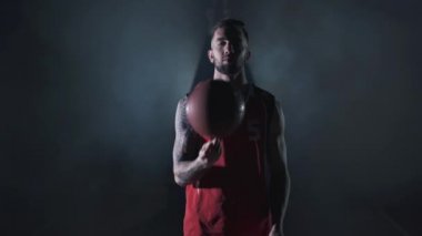 Portre genç yakışıklı sakallı acımasız kendine güvenen basketbolcu siyah arka plan üzerinde duman bulutları bir top ile standı.