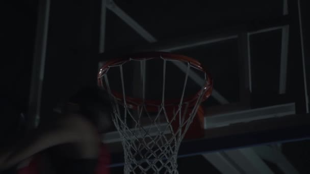Close up image of professional basketball player making slam dunk during basketball game in dark basketball court. — Stock Video