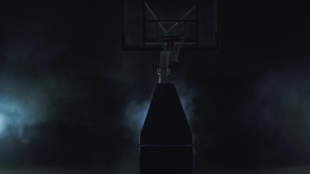 Young man in red uniform throws the ball in the basket on the dark background in the cloud of smoke and walks away. Professional basketball game player in action. Concept of sport — Stock Video