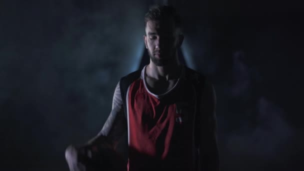 Retrato joven guapo brutal sin afeitar jugador de baloncesto seguro de pie con una pelota en las nubes de humo sobre fondo negro . — Vídeos de Stock