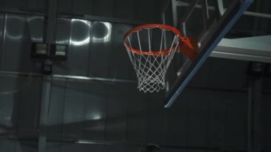Basketbolcu bir oyun sırasında bir slam dunk yapar. Markasız spor kıyafetler giyiyor..