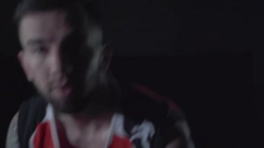 Kırmızı üniformalı yakışıklı adam bir topla yere vuruyor ve topu karanlık zeminde yönetiyor. Profesyonel basketbol oyuncusu oyuna dahil. Kamera yakınlaştırma ve uzaklaştırma