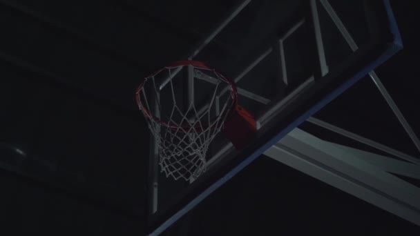 フラッドライトバスケットボールコートでバスケットボールの試合中にスラムダンクを作るプロバスケットボール選手のクローズアップ画像. — ストック動画
