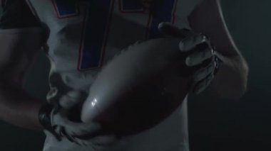 Tanınmayan Amerikan futbolcusu spor malzemeleri yle topu elinde dönen karanlık arka planda yakından takip etti. Ön görünüm