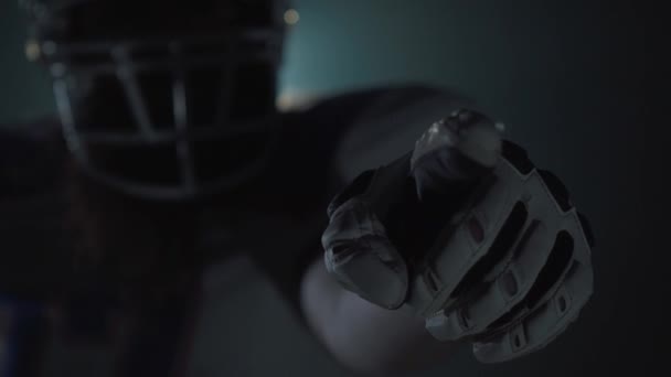 Nahaufnahme Porträt eines amerikanischen Fußballspielers in Sportausrüstung und Helm, der mit dem Finger in die Kamera zeigt, auf dunklem Hintergrund mit Scheinwerfer. Frontansicht — Stockvideo