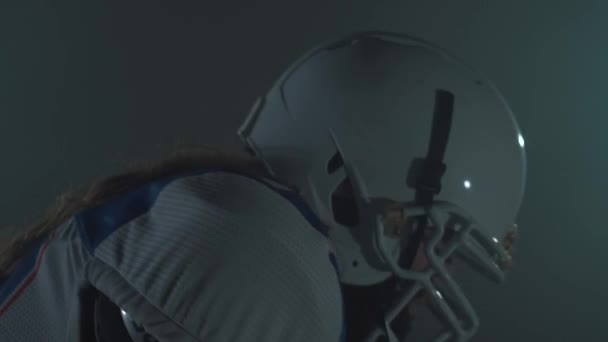 Retrato de jugador de fútbol americano barbudo en casco empezar a correr, haciendo un guion en el fondo oscuro. Concepto de masculinidad, deporte, victoria. Vista lateral — Vídeos de Stock