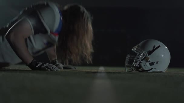 Close-up American Football speler met lang haar en baard in handschoenen liggend op de vloer te kijken op zijn helm voor het spel close-up. Concept van sport, overwinning, mannelijkheid — Stockvideo
