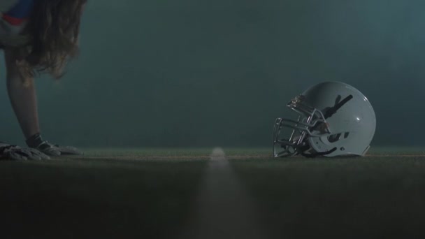 Close-up American Football speler met lang haar en baard in handschoenen liggend op de vloer te kijken op zijn helm voor het spel close-up. De man stapt op en begint te rennen. Concept van sport, overwinning — Stockvideo