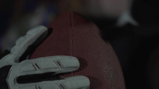 Primer plano de las manos de un atleta profesional con guantes deportivos sosteniendo una pelota de rugby . — Vídeos de Stock