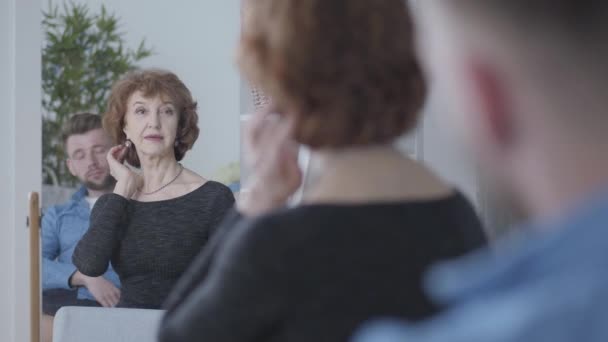 Mooie Senior volwassen vrouw kijkt in de spiegel bij haar reflectie, het aanraken van haar haar zittend in de voorkant van de jonge man in blauw shirt. Relatie tussen oudere vrouw en jongere man. Leeftijdsverschil — Stockvideo