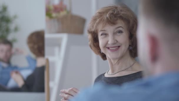 Mooie elegante rijpe vrouw praten met haar partner zittend thuis op de Bank close-up. Reflectie van twee mensen in de spiegel. Camera beweegt rechts en links — Stockvideo