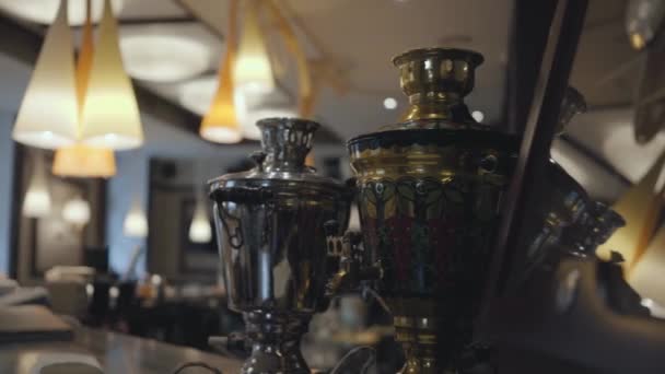 Two beautiful shiny samovars standing on the bar counter in modern pub close up. Comfortable place with beautiful rich decoration. Camera moving left and right — Stock Video