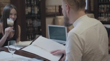 Glamour esmer kadın onu dinlerken onu dinleyen ve gülümseyerek onu sakallı erkek arkadaşı ile masada oturan kokteyl içme ve adam menüde çanak seçerken. Sevimli çiftin bir randevusu var. Kamera hareketli