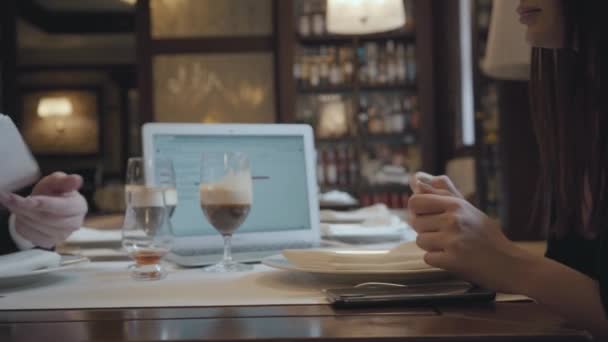 Невпізнаваний чоловік і жінка сидять за столом у кафе, працюючи. Ноутбук, папери та окуляри з кавою на столі. Чоловік передає папір партнеру. Зустріч зі співробітником — стокове відео