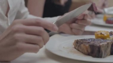 Ön planda genç adam ve arka planda kadın restoranda yaprakları ve sebze ile tabakta yatan lezzetli biftek kesme elleri. Sevimli çiftin bir randevusu var. Kamera sağa hareket ediyor
