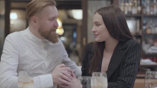 Jolie jeune femme et un beau blond barbu assis à la table. L'homme qui dit de bonnes paroles à sa copine. Le couple mignon a un rendez-vous . — Video