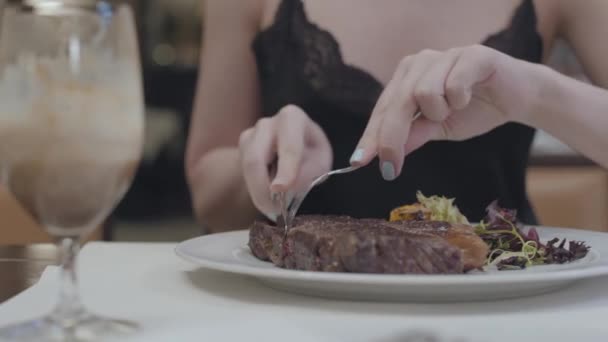 Kezében fiatal nő vágás ízletes steak feküdt zöldségek és levelek a tányéron az étteremben. Alkoholos üveg állandó közelében. Kameramozgás jobb — Stock videók