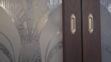 Ceketli tanınmayan adam sürgülü kapılara giriyor ve arkasından kapıları kapatıyor. Güzel iç detaylar
