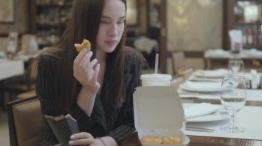 Genç ve güzel bir kadın pahalı bir restoranda oturuyor ve kola ile tavuk nugget yiyor.
