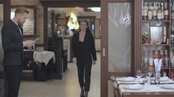 Mannelijke en vrouwelijke zakenpartners ontmoeten elkaar in het restaurant. Mensen schudden de handen. Dame in een elegant pak komt naar de bebaarde man te wachten voor haar in de buurt van de ingang — Stockvideo