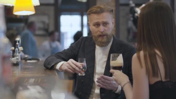 Brunette vrouw en zelfverzekerde blonde bebaarde man zittend aan de bar teller close-up. Concept van nachtleven. Schattig paar heeft een datum. — Stockvideo