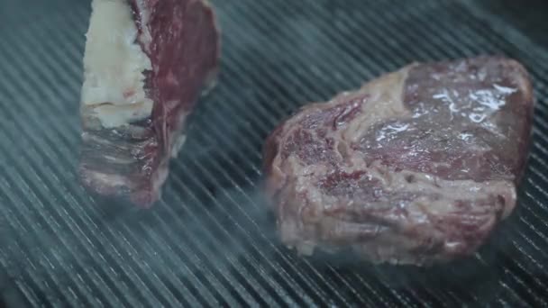 Läckra saftiga biff biffar liggande på grillen ytan närbild. Två bitar av rått kött förbereder sig i restaurangköket. Kocken förbereder god mat — Stockvideo