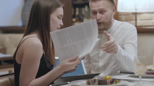 Portret jonge vrouw en blond bebaarde man zittend aan de tafel in het café bespreken van documenten. De man houdt laptop. Ontmoeting met medewerker — Stockvideo