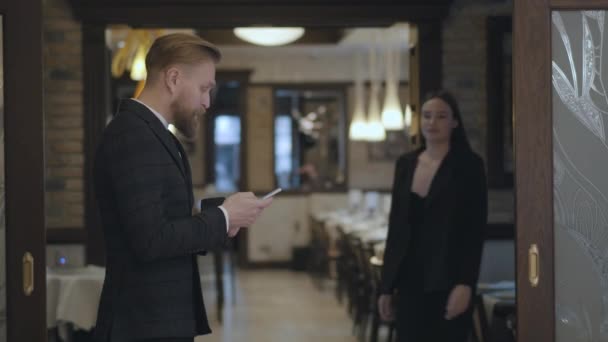 Socios de negocios masculinos y femeninos se reúnen en el restaurante. Gente dándose la mano. Dama en un traje elegante que viene al hombre barbudo esperándola cerca de la entrada — Vídeos de Stock