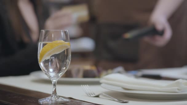 Vidrio con agua y limón en el restaurante de la mesa y en el fondo es una mujer pagar factura de cheque — Vídeos de Stock