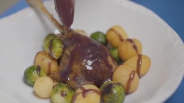 Beyaz tabakta ördek bacağı, patates topları ve sosis filizleri.