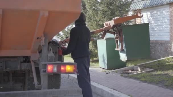 Vista posteriore dell'uomo che controlla il lavoro della macchina della spazzatura. L'operaio in abiti casual si mette il cassonetto usando la macchina della spazzatura — Video Stock