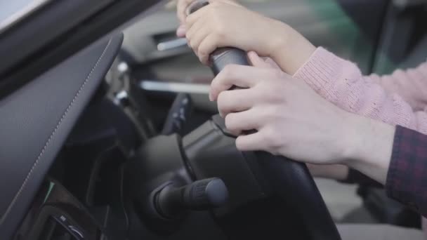 Papá le enseña a su pequeña y linda hija a girar el volante sentado en su coche en el asiento del conductor. De cerca. — Vídeos de Stock